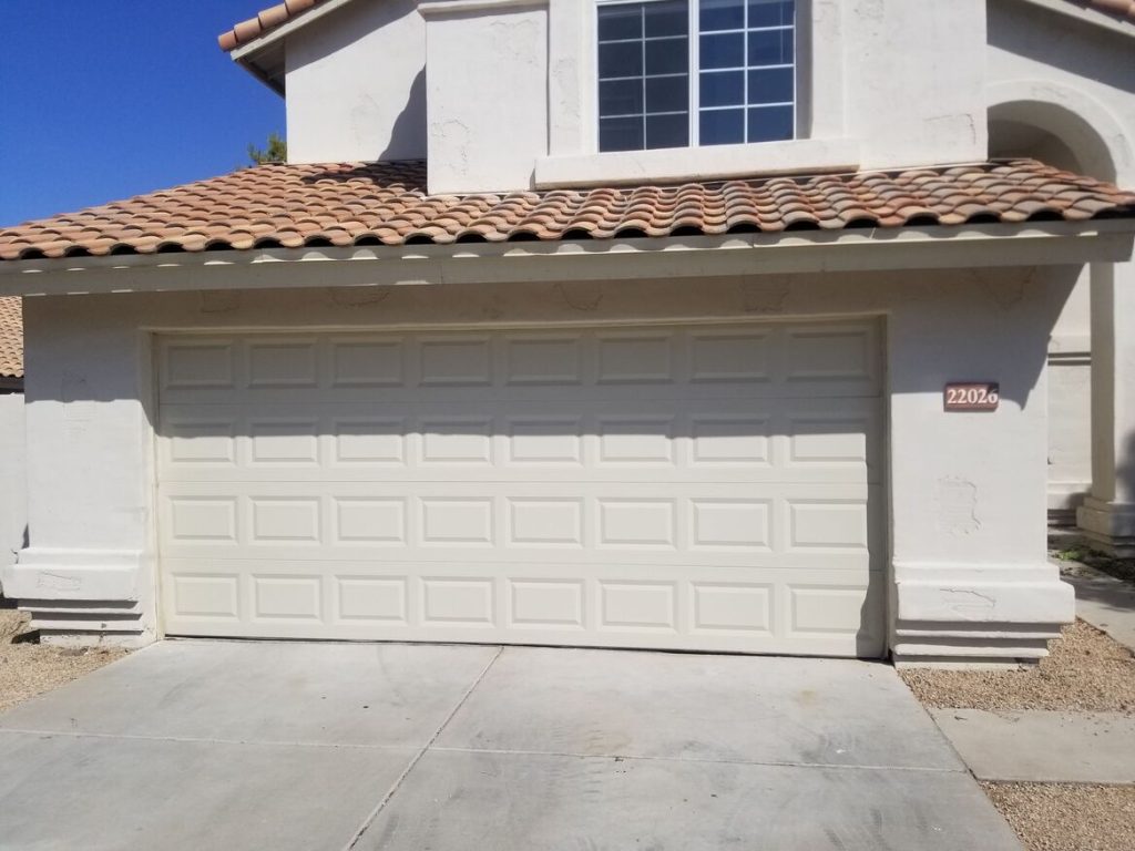 A white garage door with a textured pattern, flanked by light-colored walls and a tiled roof, featuring a house number plaque of 2202.
