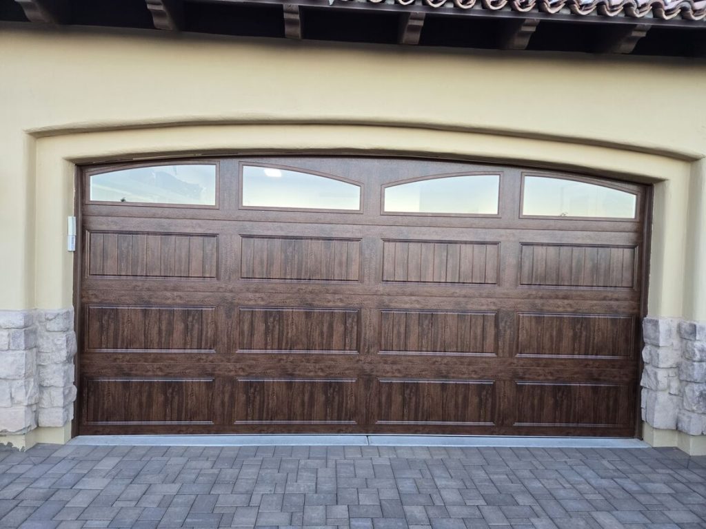 A classic wooden garage door with a rich brown finish and decorative windows, framed by light-colored stone and a stucco wall.