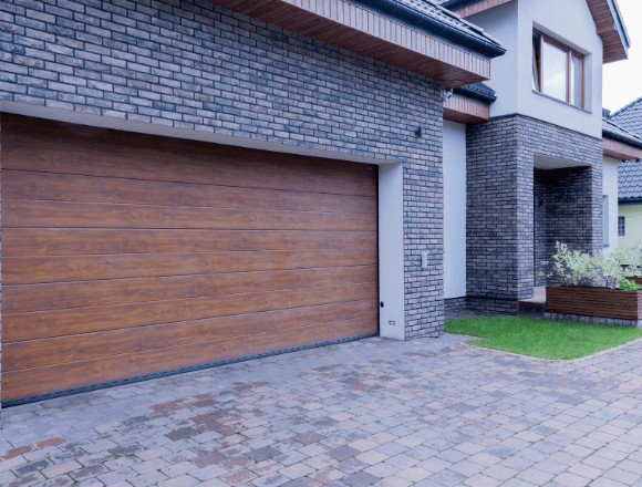 Modern house exterior featuring a large wooden garage door, stone brick facade, and a manicured front yard with greenery.