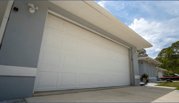 A close-up view of a modern white garage door against a light gray house, with a clear blue sky above and landscaping to the side.