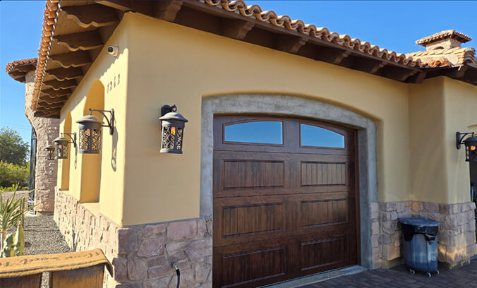 Close-up of a Mediterranean-style home exterior featuring a wooden garage door, stone accents, and decorative lanterns under a tiled roof.