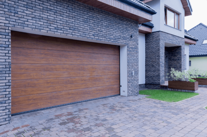 A modern house exterior featuring a large wooden garage door, gray brick walls, and a small patch of green grass.